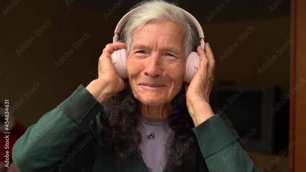 Old woman uses wireless earphones. Old person and technologies. Village pensioner, listens to