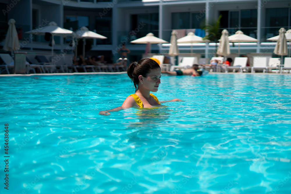 young female person in yellow swimsuit swimming in the pool, summer resort vacation