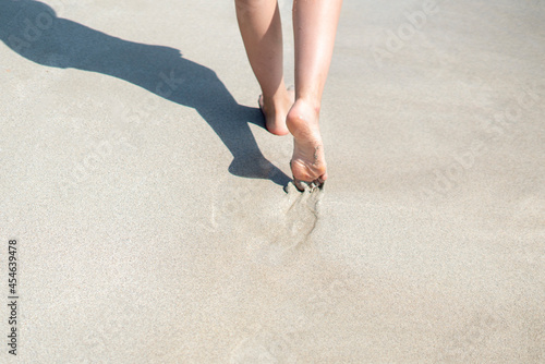 view from behind of a person walking on the sandy sea beach with bare feet