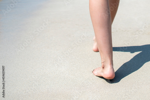 view from behind of a person walking on the sandy sea beach with bare feet