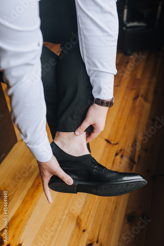 A stylish man businessman in a white shirt puts on black shiny shoes on his feet, going to work in the morning. Business photography.