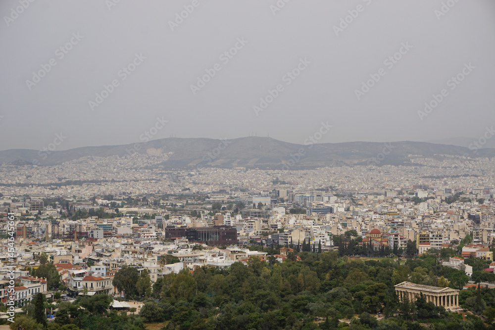 Athens, Greece: View from the Acropolis of the Doric Temple of Hephaestus and the Athens skyline, under a hazy sky caused by dust pollution.