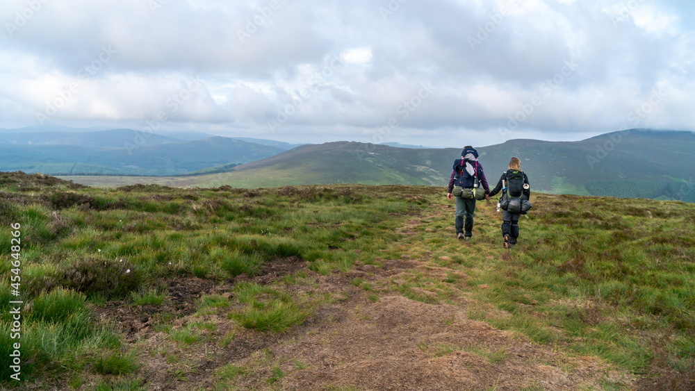 Hiking trail in Wicklow, Irish mountains region. Two hikers men walk on trek in mountain. Tourists with backpacks hike in highlands. Trekking in mountains. Hills and mounts in sport tourism.