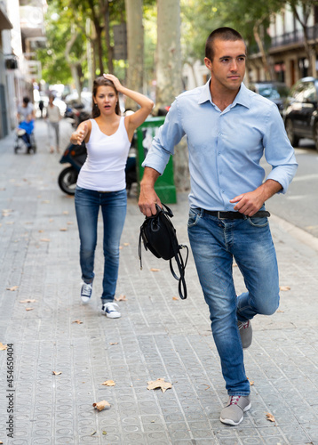 Male thief stealing bag from scared woman on street