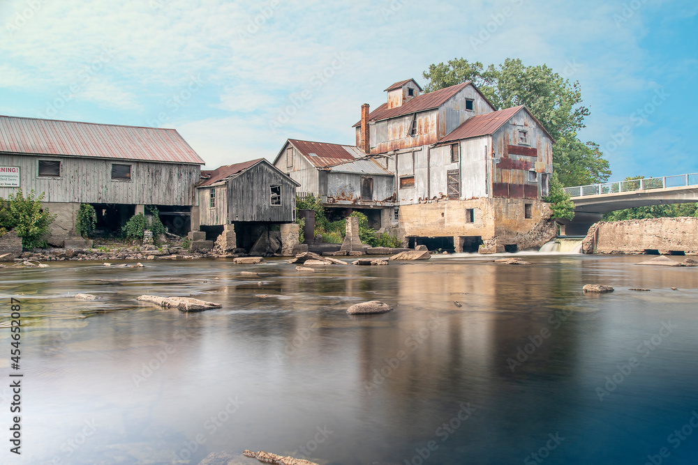 A historic mill sits by the glassy waters of a river on a beautiful sunny day in Chisholm, Ontario.