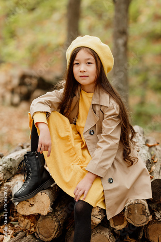 a little brunette Asian girl in autumn clothes walks in the autumn forest near a stream. High quality photo