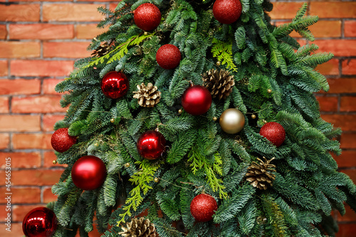 Fir tree decorated with christmas balls over red brick wall . Close-up view of beautiful christmas tree with colorful baubles and illuminated garland. Sparkling and fairy background. New year holiday