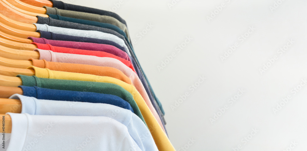 close up collection of color t-shirts hanging on wooden clothes hanger in closet or clothing rack over white background, copy space close up collection of color t-shirts hanging on wooden clothes hanger in closet or clothing rack over white background, copy space