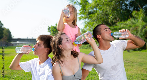 Parents with teenager son and daughter drinking cold water from plastic bottles in summer park. High quality photo