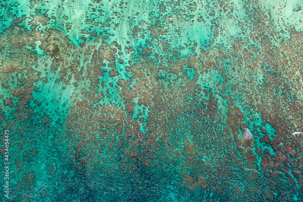 Abstract aerial view of coral reef in Oahu, Hawaii. Water has blue and green shades, reef is brown.
