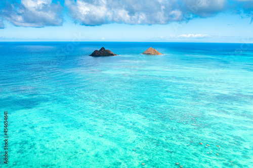 Aerial drone view of the Mokolua islands off the coast of Lanikai Beach in Oahu, Hawaii, USA. Water is turquoise, reef is visible, few white clouds in sky. 