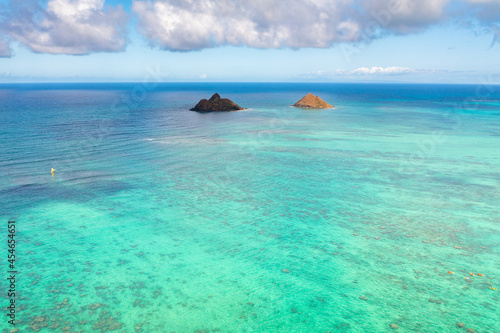 Aerial drone view of the Mokolua islands off the coast of Lanikai Beach in Oahu, Hawaii, USA. Water is turquoise, reef is visible, few white clouds in sky. 