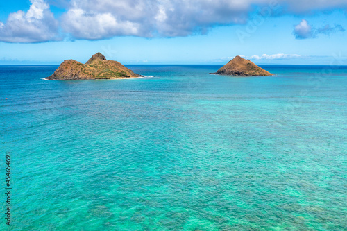 Aerial drone view of the Mokolua islands off the coast of Lanikai Beach in Oahu, Hawaii, USA. Water is turquoise, reef is visible, few white clouds in sky.	 photo