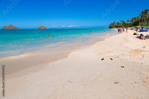 Landscape view of the twin brown Mokolua islands "Mokes" off the coast of Lanikai Beach in Oahu, Hawaii, USA. White sand beach, turquoise water, copy space in clear blue sky. A few people in water.