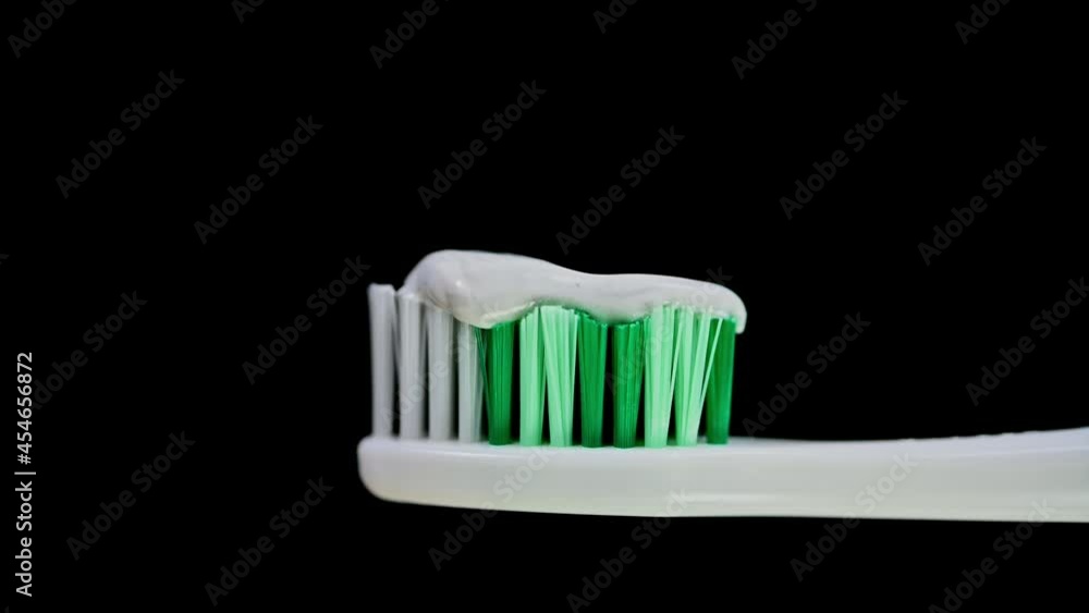 A zoom out of a toothbrush with white and green bristles loaded with toothpaste revealing a dark background. A zoom out of a toothbrush with white and green bristles loaded with toothpaste revealing a dark background.