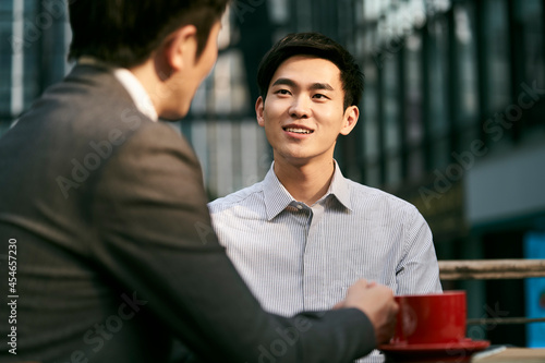 two asian business men meeting talking chatting in outdoor cafe