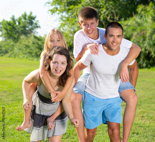 Cheerful friendly family having fun together in summer city park, parents piggybacking children