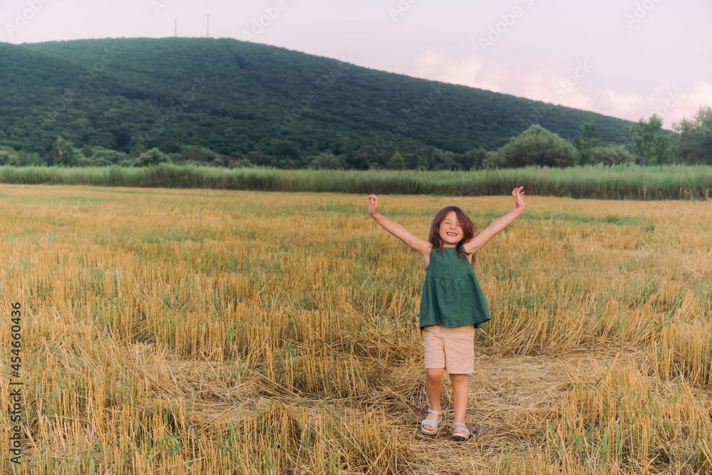 Happy little girl celebrating, holding out her hands in a yellow field. High quality photo