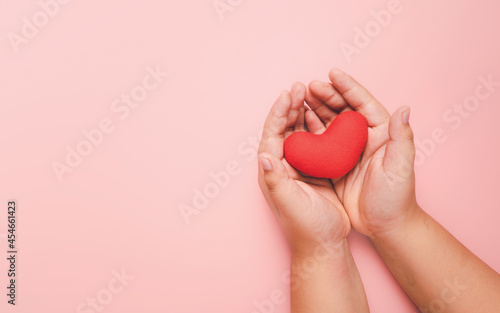 Fototapeta Naklejka Na Ścianę i Meble -  Little boy hand holding red heart on pink background, health care, love, organ donation, family insurance,CSR,world heart day, world health day, praying concept, Top view.