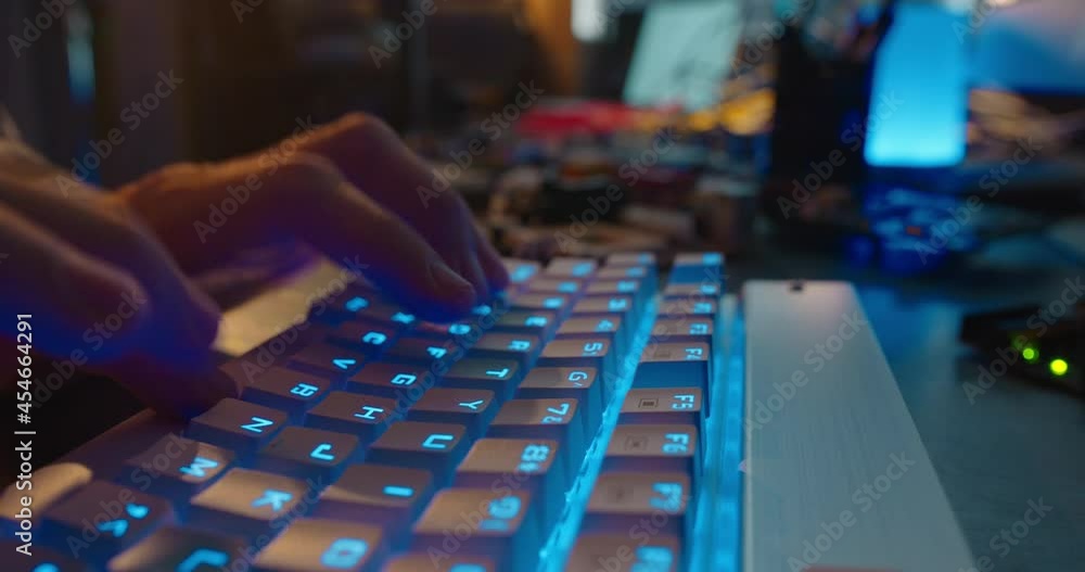 computer hands typing on keyboard browsing online gaming late at night using keyboard with blue backlight