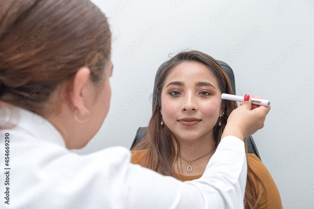 Young woman affected of the eyes by computer screens and telephones. The ophthalmologist performs a visual diagnostic examination of the left eye of a young woman who is sitting Young woman affected of the eyes by computer screens and telephones. The ophthalmologist performs a visual diagnostic examination of the left eye of a young woman who is sitting
