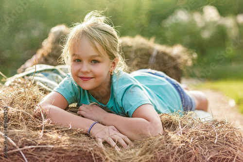 Portrait of a smiling 9-year-old blonde girl lying on a haystack. Happy childhood. A hot summer evening.