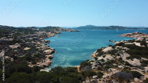 Aerial of an idyllic natural coast beach rock bay at La Maddalena on the tourist vacation island Sardinia in Italy with sun, clear blue turquoise and calm water. Beautiful drone air view flight.