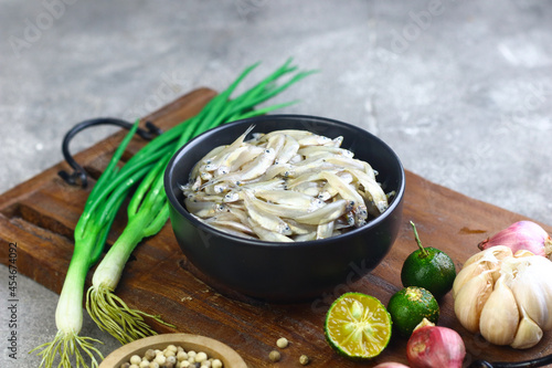Ikan Teri Basah or fresh anchovies on black ceramic bowl with some raw ingredients. Indonesian fish from sea.  photo