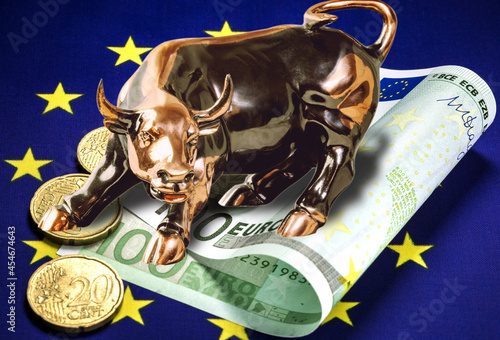 Concept of European trading. 100 euro bill, euro coins lying on the european community flag. Brass bull standing on euro coins. Macro image.