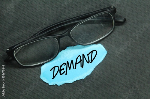 glasses, torn paper with the word demand photo