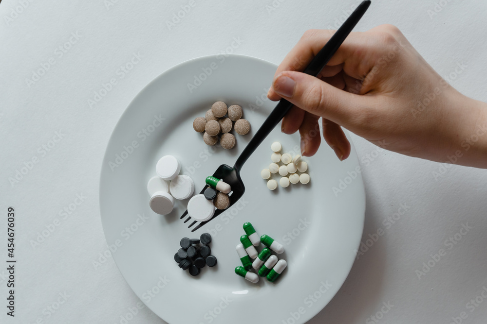 nutritional supplement pills and tablets on white plate with black fork and knife nutritional supplement pills and tablets on white plate with black fork and knife
