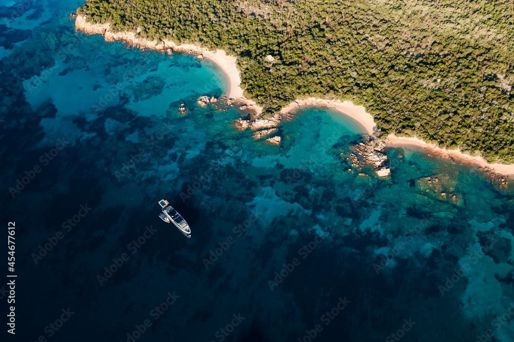 View from above, stunning aerial view of a green coastline with some beautiful beaches and a yacht sailing on a turquoise water. Liscia Ruja, Costa Smeralda, Sardinia, Italy.