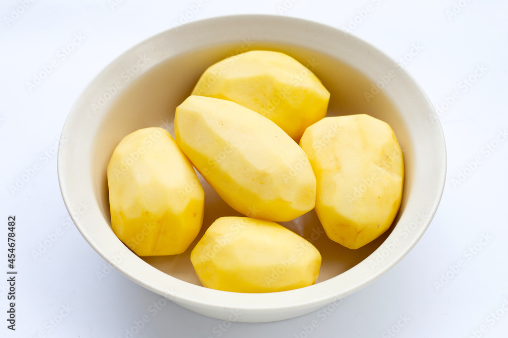 Raw peeled potatoes in white bowl on white background