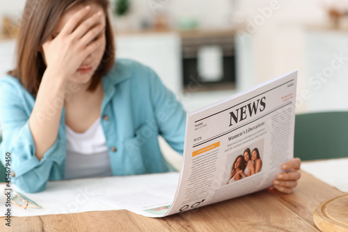 Upset young woman reading newspaper at home
