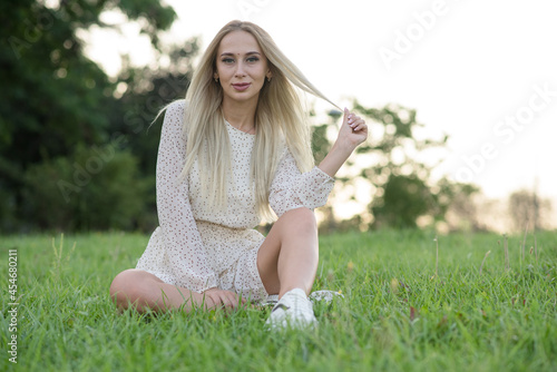 Portrait of a happy and attractive blonde girl sitting on green grass.