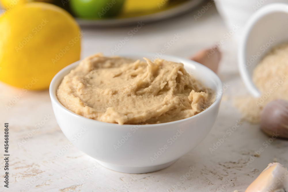 Bowl with tasty hummus on light background, closeup