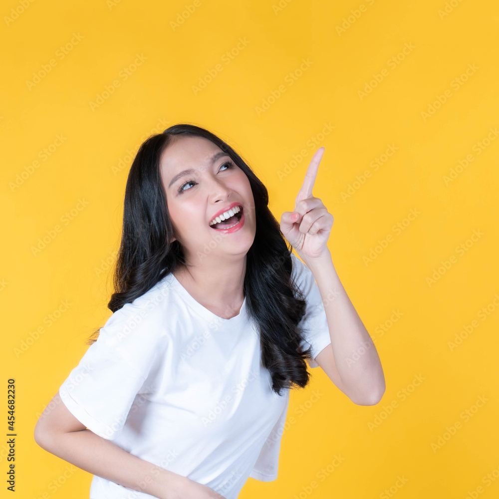 beautiful cute Asian woman smiling and pointing finger to empty copy space , blank space for advertising isolated on yellow background beautiful cute Asian woman smiling and pointing finger to empty copy space , blank space for advertising isolated on yellow background