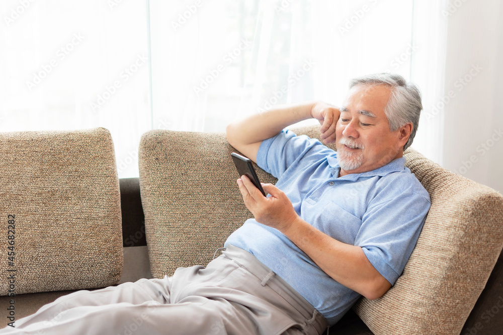 Senior Male using a smartphone , smiling feel happy on sofa at home - lifestyle senior concept