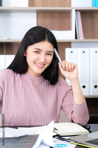 Portrait of Asian business young woman company employee on office desk and pointed a finger to her head , thinking about how to make money online from the money- lifestyle business people concept