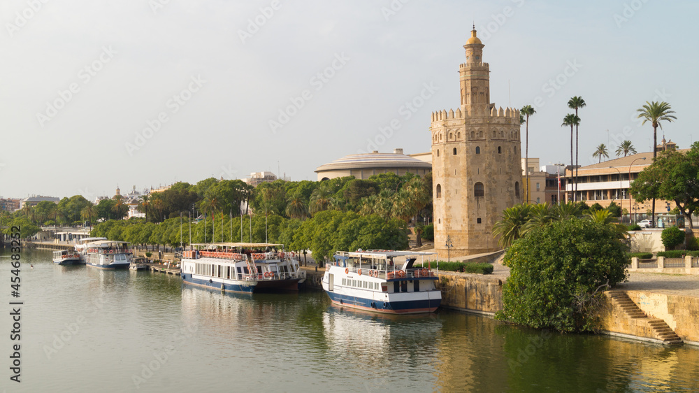 Urban landscape of the city of Seville with views of the promenade along the Guadalquivir river, the tourist cruises and the Torre del Oro.