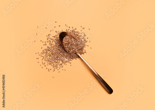 Spoon with flax seeds on color background