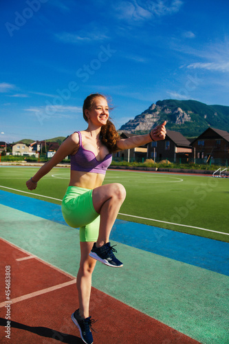 A sporty woman runs through the stadium. A girl trains on a treadmill. Sportswear. A bright sunny day and a blue sky.