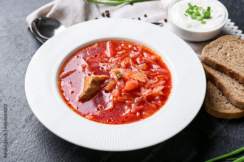 Plate of tasty borscht, sour cream and bread on dark background Plate of tasty borscht, sour cream and bread on dark background