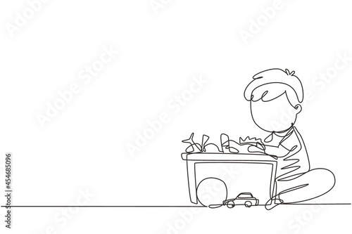 Single continuous line drawing little boy putting his toys into box. Kids doing housework chores at home concept. Smiling child storing his toys in the box. Dynamic one line draw graphic design vector