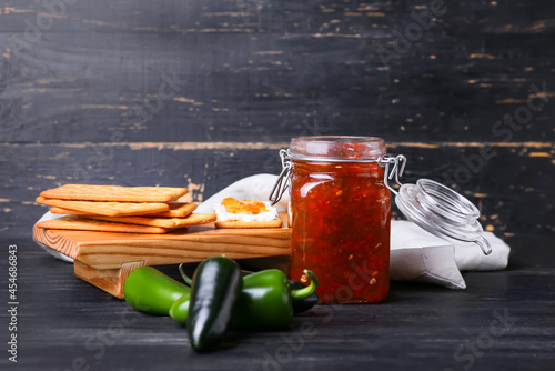 Jar with delicious jalapeno pepper jam and crackers on dark wooden background photo