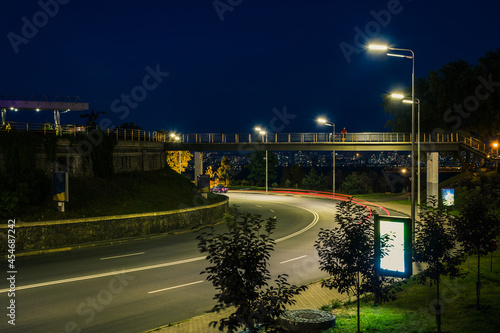 Night road with traffic in the city. Small footbridge over the highway at night. City road viaduct streetscape of night scene