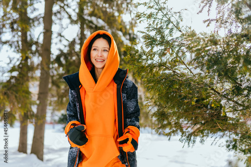Midlle age slim brunette woman enjoy freezing day take exercises, walking wearing warm orange sportswear in city park outdoors.