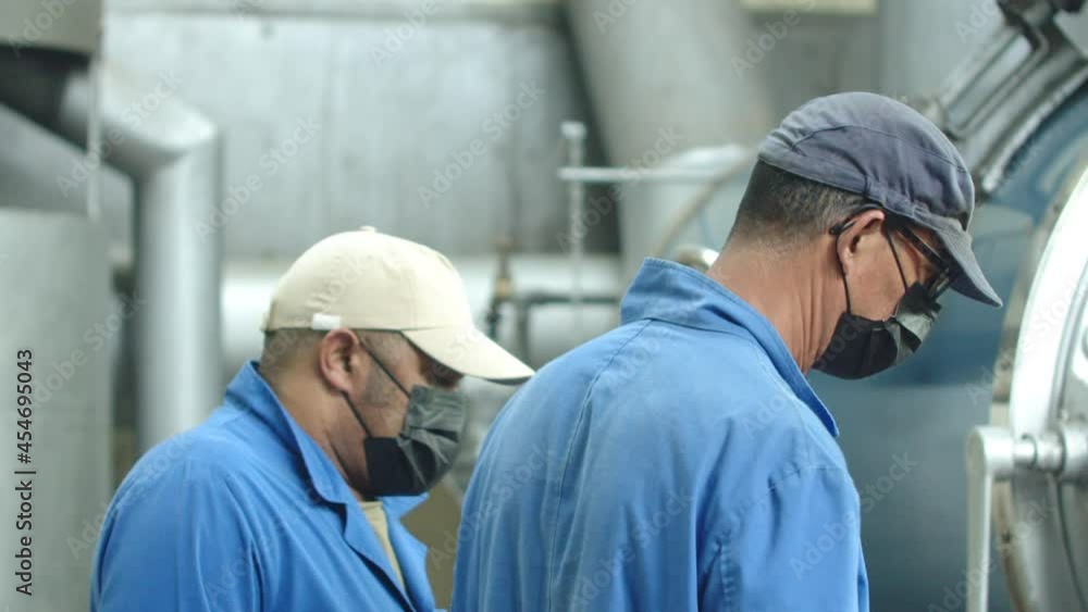 Slow motion of male laborers working at factory. Men in uniform, caps and masks operating coffee roasting machine. Working together, partnership, occupation concept Slow motion of male laborers working at factory. Men in uniform, caps and masks operating coffee roasting machine. Working together, partnership, occupation concept