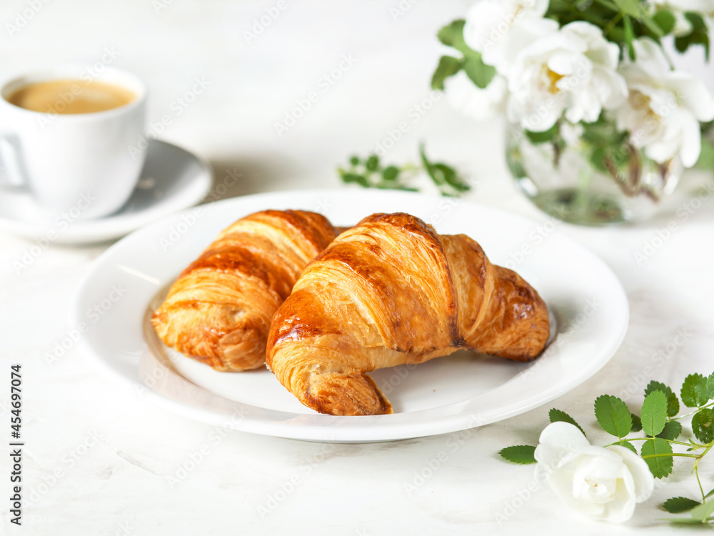 Serving breakfast on a marble table. Croissants on a white plate. French cuisine. Pastries, coffee and white flowers. It's a beautiful morning. French-style breakfast for a girl Serving breakfast on a marble table. Croissants on a white plate. French cuisine. Pastries, coffee and white flowers. It's a beautiful morning. French-style breakfast for a girl