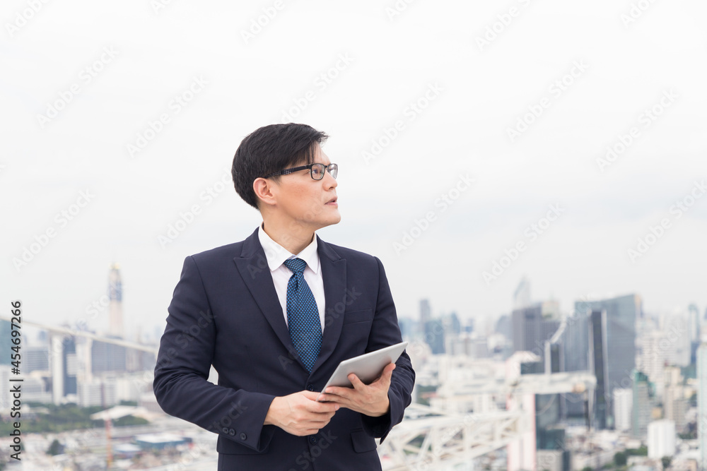 Asian businessman in formal suit using digital tablet on rooftop with cityscape view background Asian businessman in formal suit using digital tablet on rooftop with cityscape view background